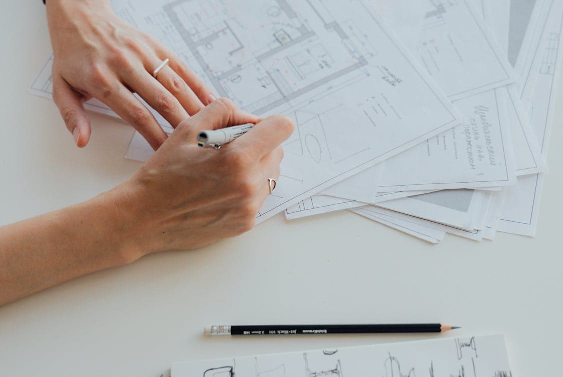 a person writing on a floor plan - 5 Benefits of Working With a Full-service General Contractor